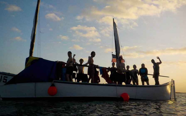 the silhouette of a group of people on a sailboat at sunset